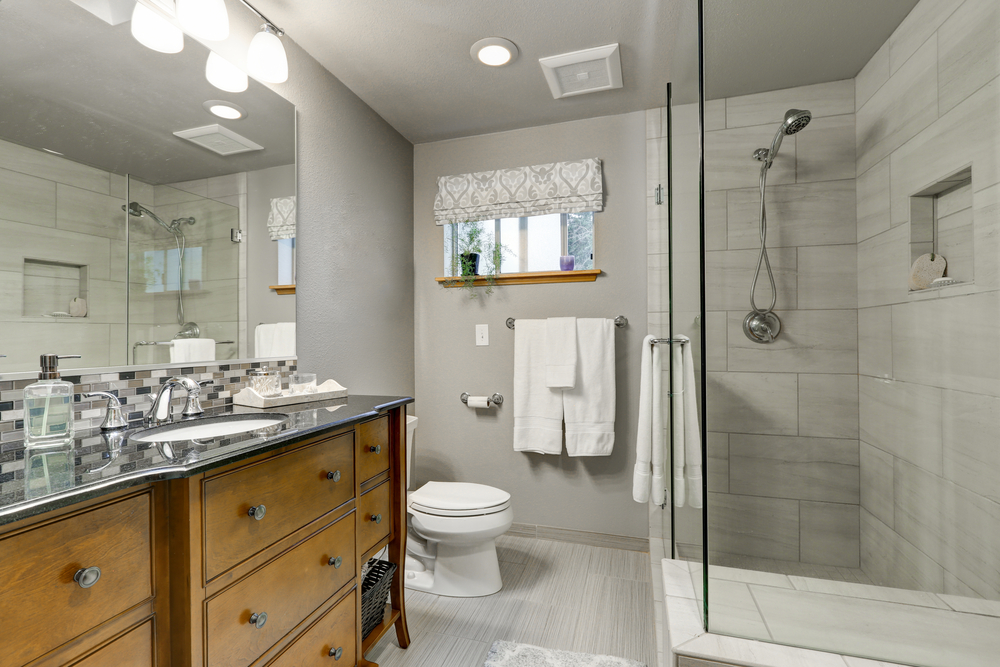 Grey bathroom interior with glass walk in shower and vanity cabinet with drawers and lower open shelves . 