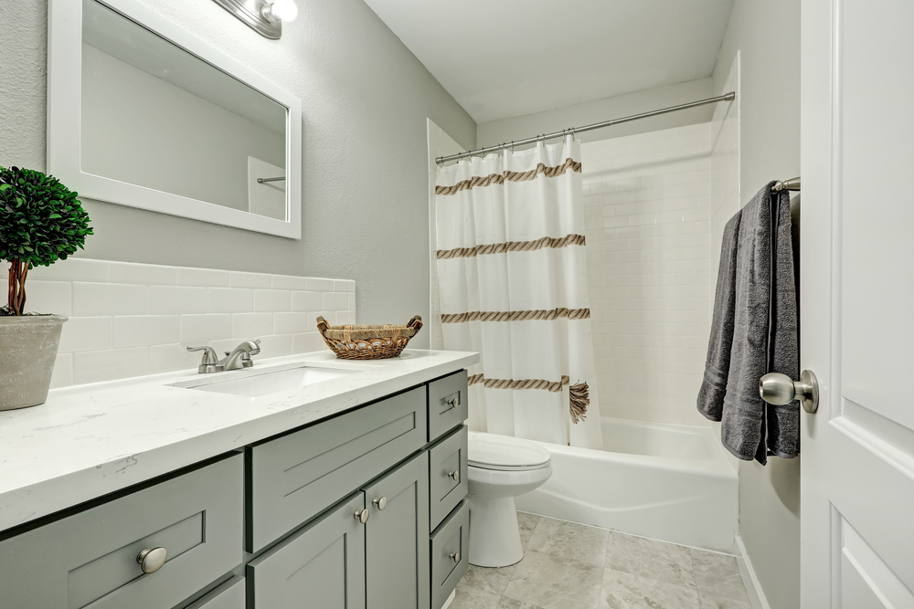 New bathroom interior boasts silver grey vanity cabinet topped with marble counter top and white backsplash.