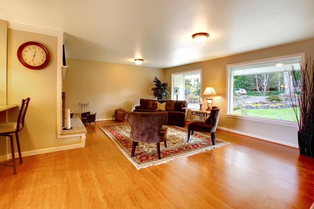 Elegant furnished living room with wide windows and hardwood floor. Brown velvet couch with chairs match light tones walls and ceiling